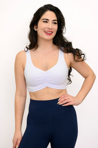 Woman wearing a white bralette and navy leggings on a white background, front view