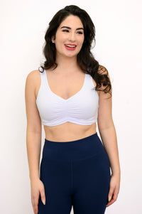 Woman wearing a white bralette and navy leggings on a white background, front view
