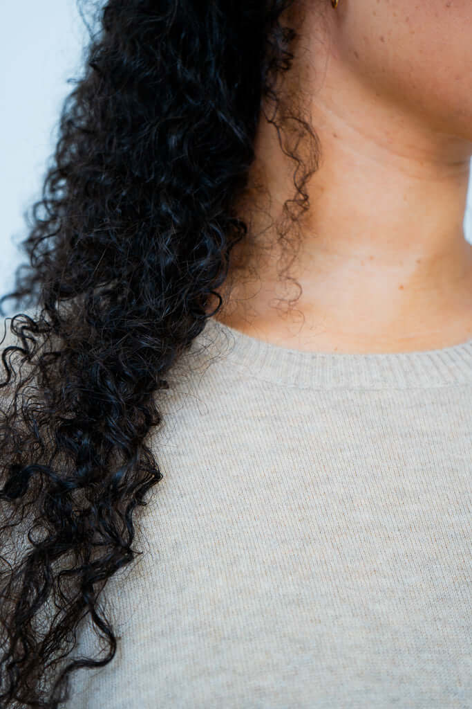 Close-up of beige sweater crew neckline and curly hair