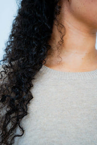 Close-up of beige sweater crew neckline and curly hair