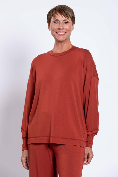 Close-up of woman wearing relaxed crew neck bamboo long sleeve top in rust color