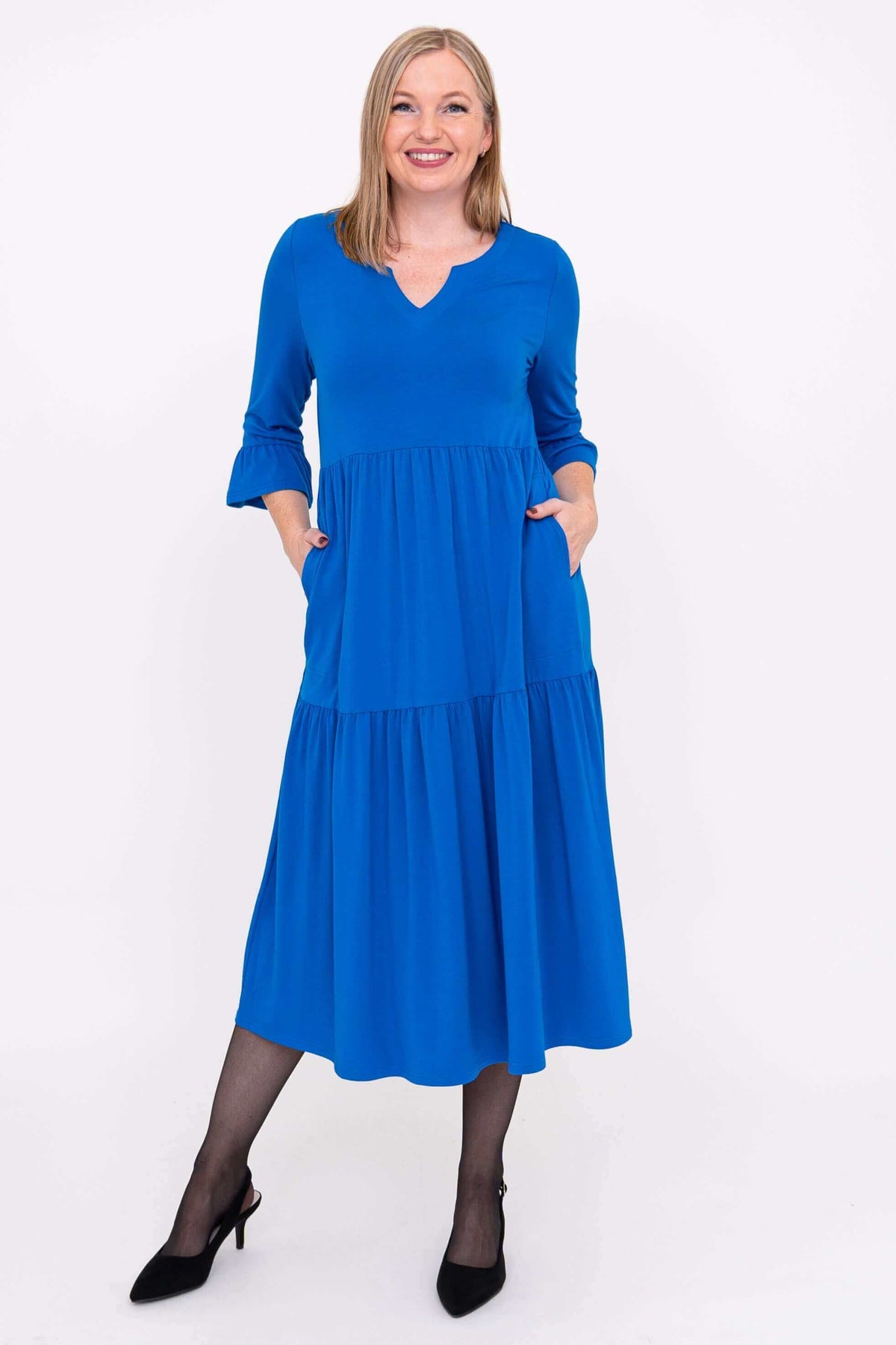 Model smiling in vibrant blue, tiered long dress, close front view
