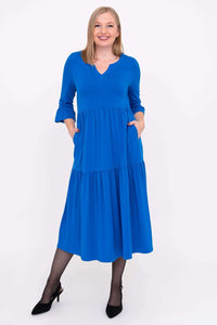 Model smiling in vibrant blue, tiered long dress, close front view