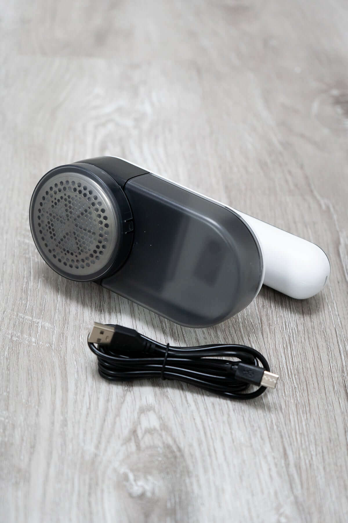 Compact electric lint remover with USB charging cable on light wood surface