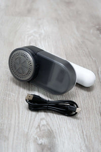 Compact electric lint remover with USB charging cable on light wood surface