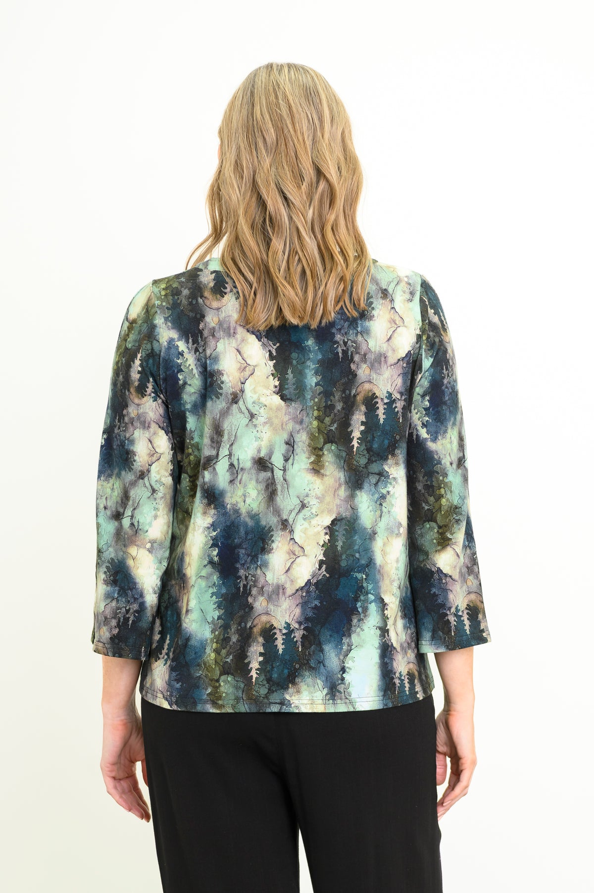 Back view of a women's green leaf patterned long-sleeve bamboo top styled with black pants.