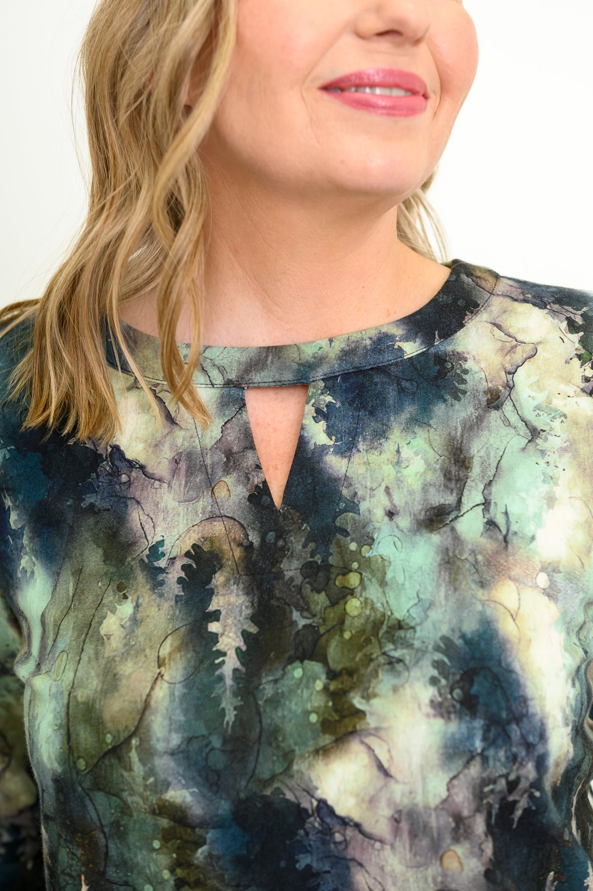 Close-up of a green forest patterned top highlighting the unique notched neckline that blends a V-neck and crew neck.