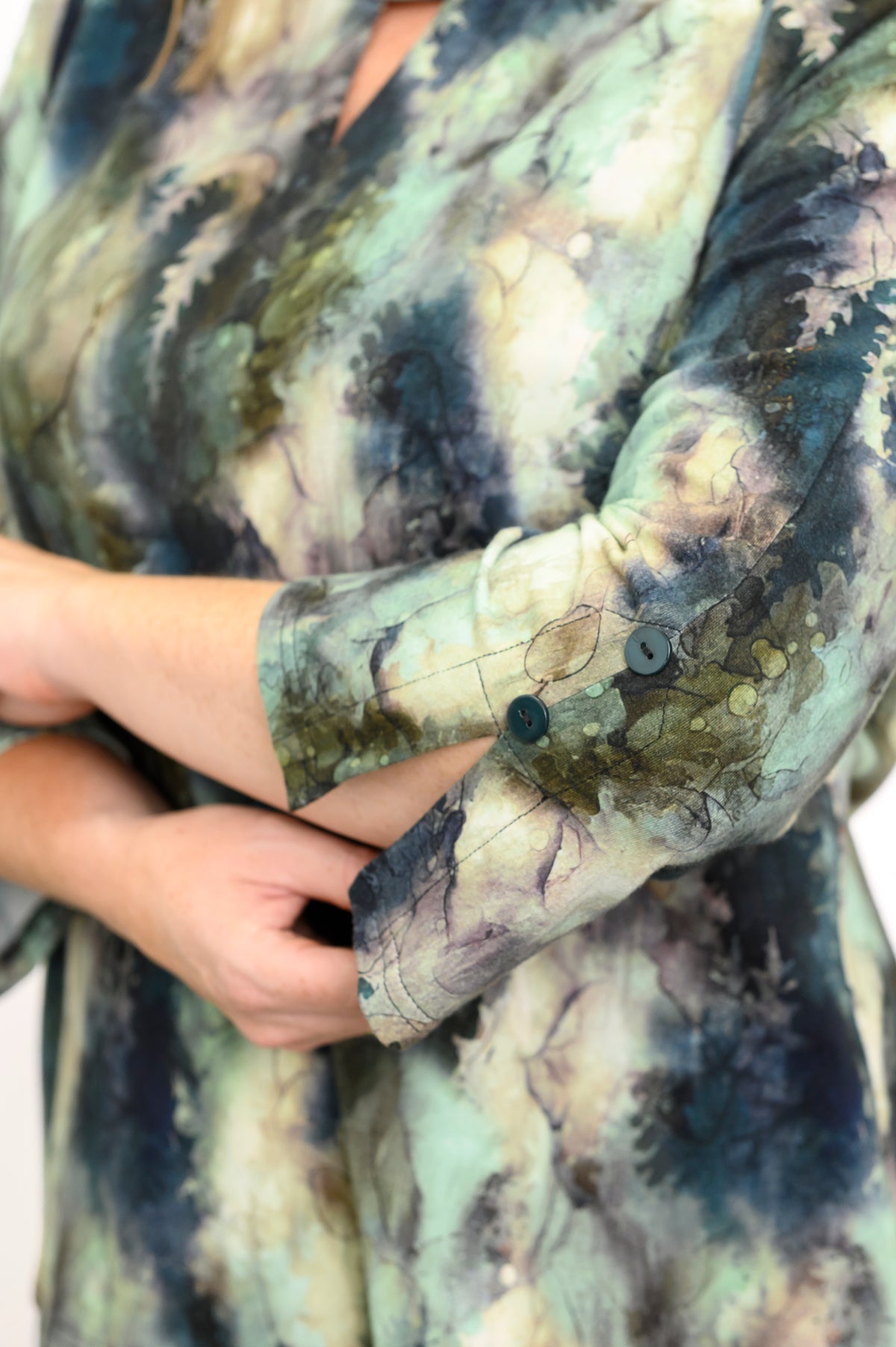 Close-up of a person wearing a long-sleeve green watercolor-style top against a white backdrop
