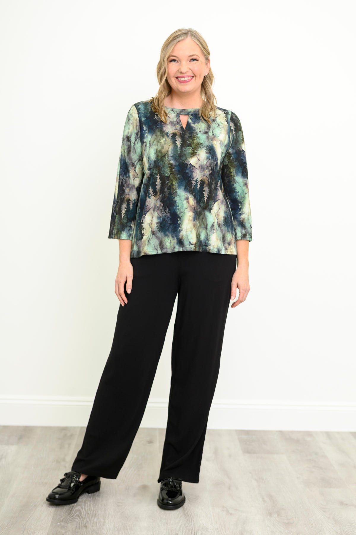 Front view of a green patterned long-sleeve knit blouse styled casually with black pants.