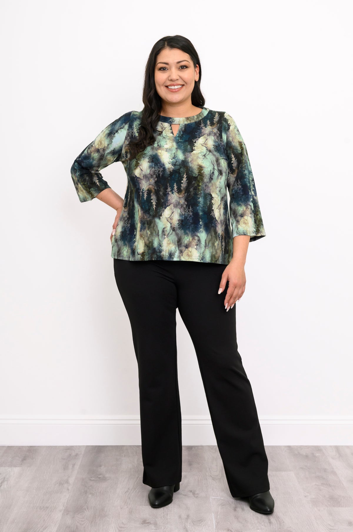 Full-body shot of a patterned green knit top with 3/4 bell sleeves and black trousers, showing the hip-length hem.