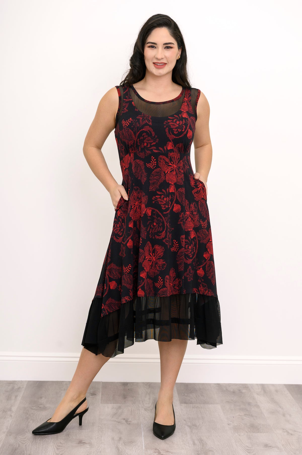 Model posing in a red and black botanical print midi dress showing a layered mesh hemline, front-facing view.