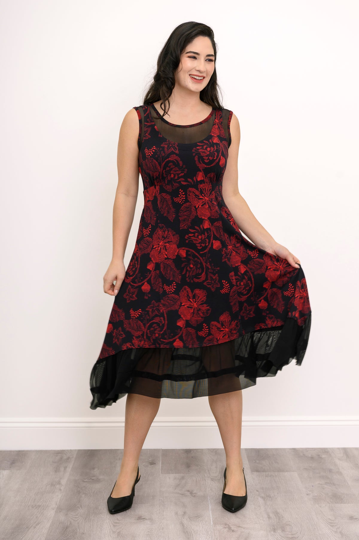 Model posing at an angle in a sleeveless red floral knit dress, highlighting the flowing, flouncy A-line skirt.