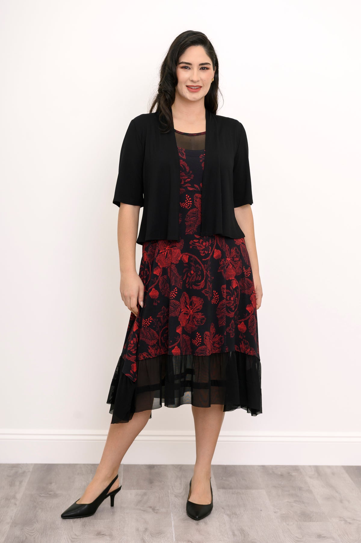 Smiling woman wearing a long-sleeve black knit sweater layered over a red floral print midi dress, front view.