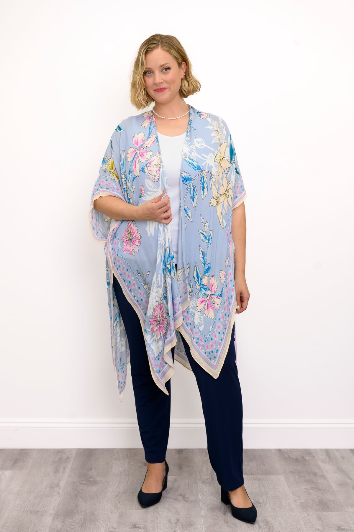 Front view of woman wearing a light blue floral kimono on a white top and navy pants against a white background