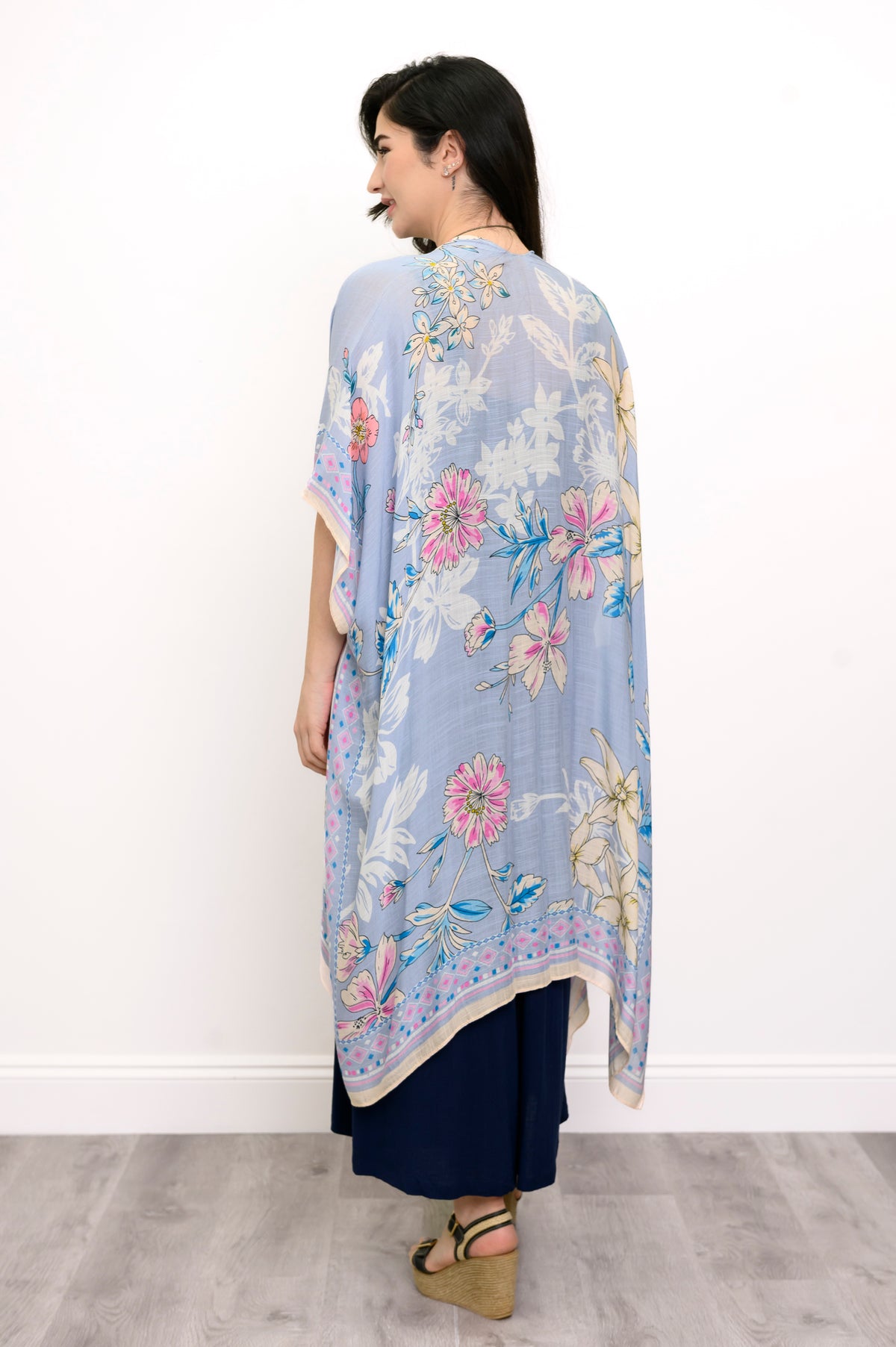 Back view of woman wearing a light blue floral kimono on a navy outfit against a white background