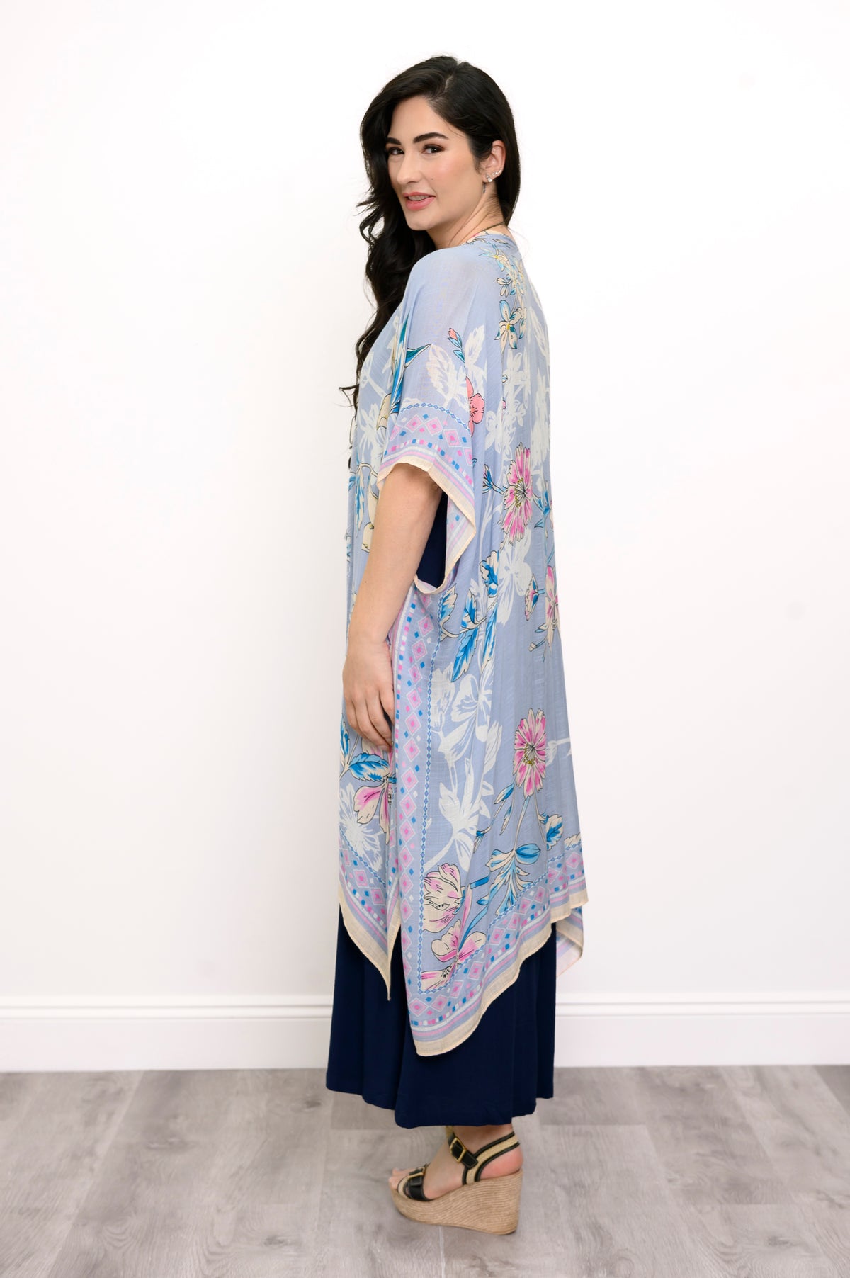 Side view of woman wearing a light blue floral kimono on a navy outfit against a white background