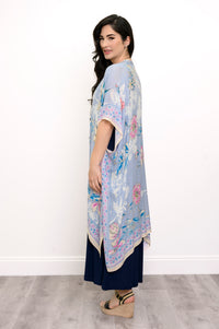 Side view of woman wearing a light blue floral kimono on a navy outfit against a white background