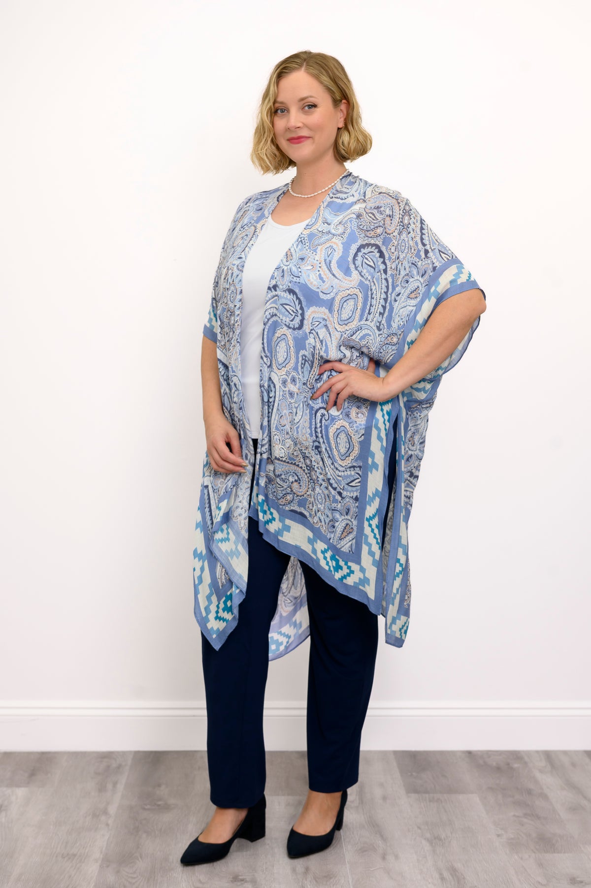 Front view of woman wearing blue paisley patterned kimono on white top outfit against a white background 