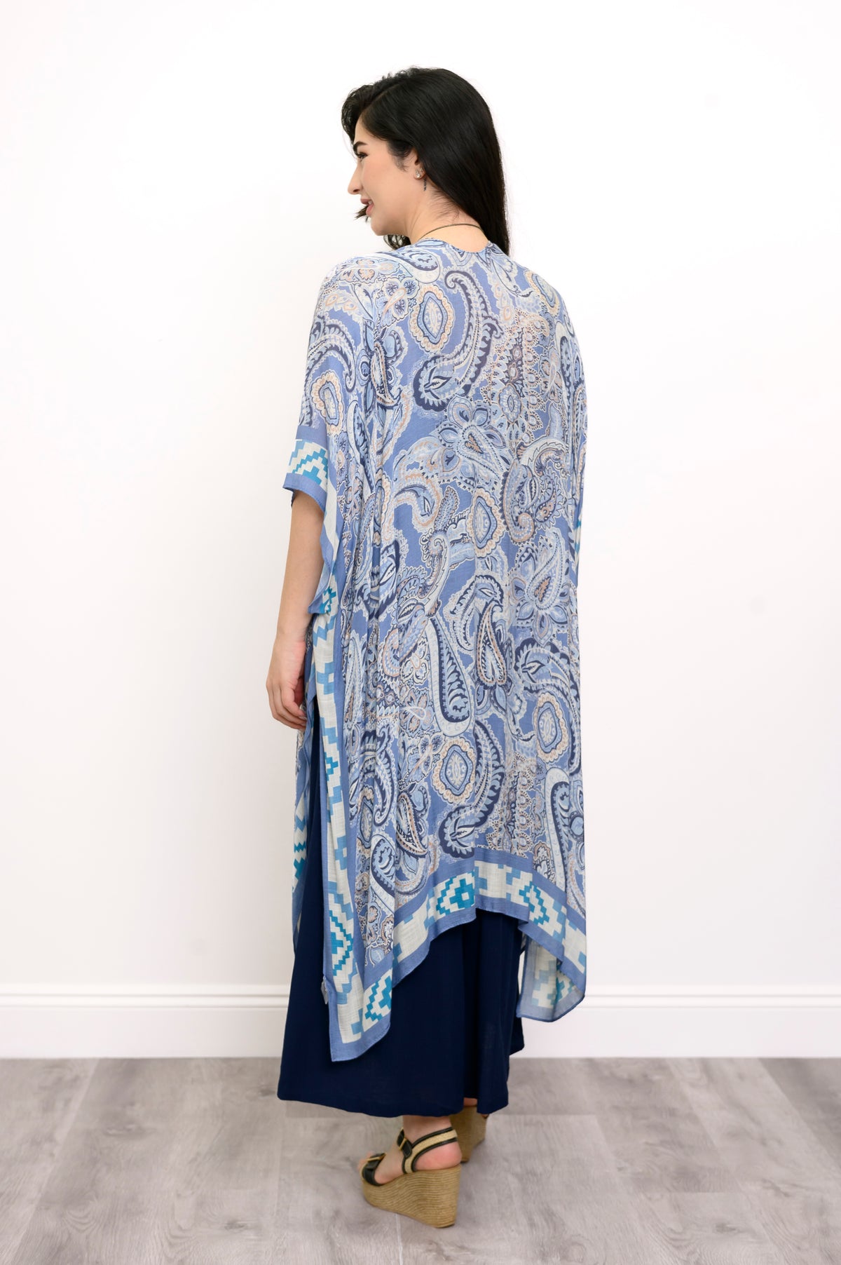 Back view of woman wearing blue paisley patterned kimono on a blue outfit against a white background 
