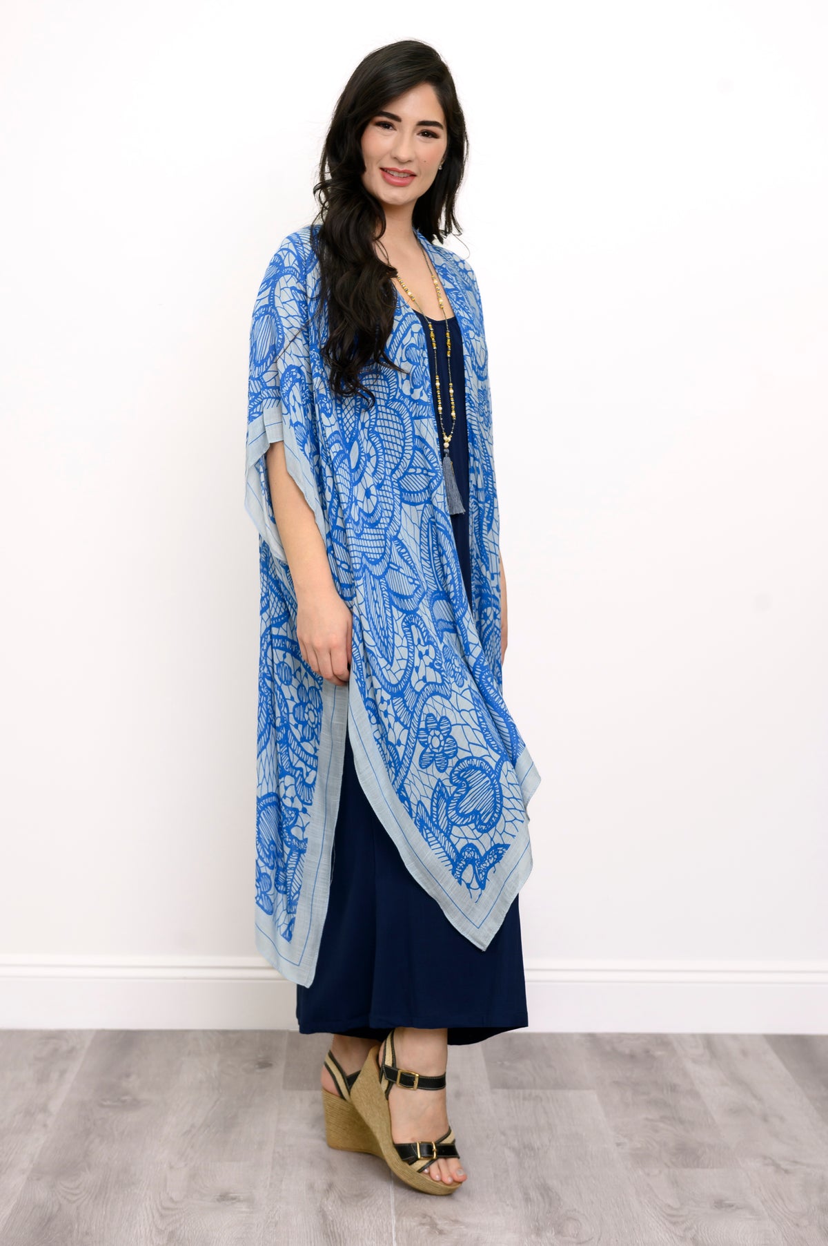 Side view of woman wearing blue lace patterned kimono on navy blue outfit against a white background 