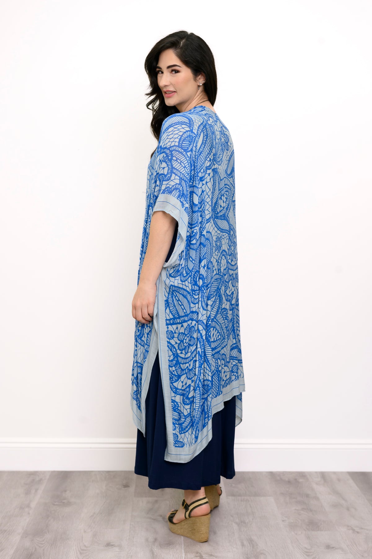 Side view of woman wearing blue lace patterned kimono on navy blue outfit against a white background 