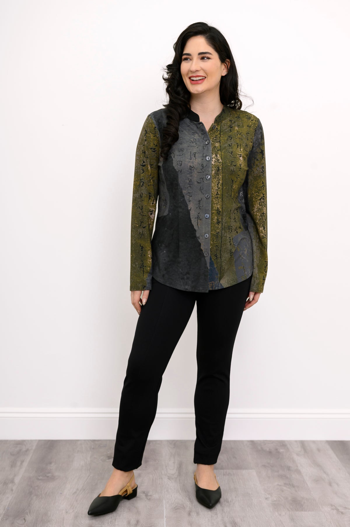 Woman wearing a green and grey patterned top and black pants on a white background, front view