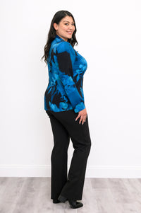 Woman wearing a blue and black floral patterned blouse and black pants on a white background, side view