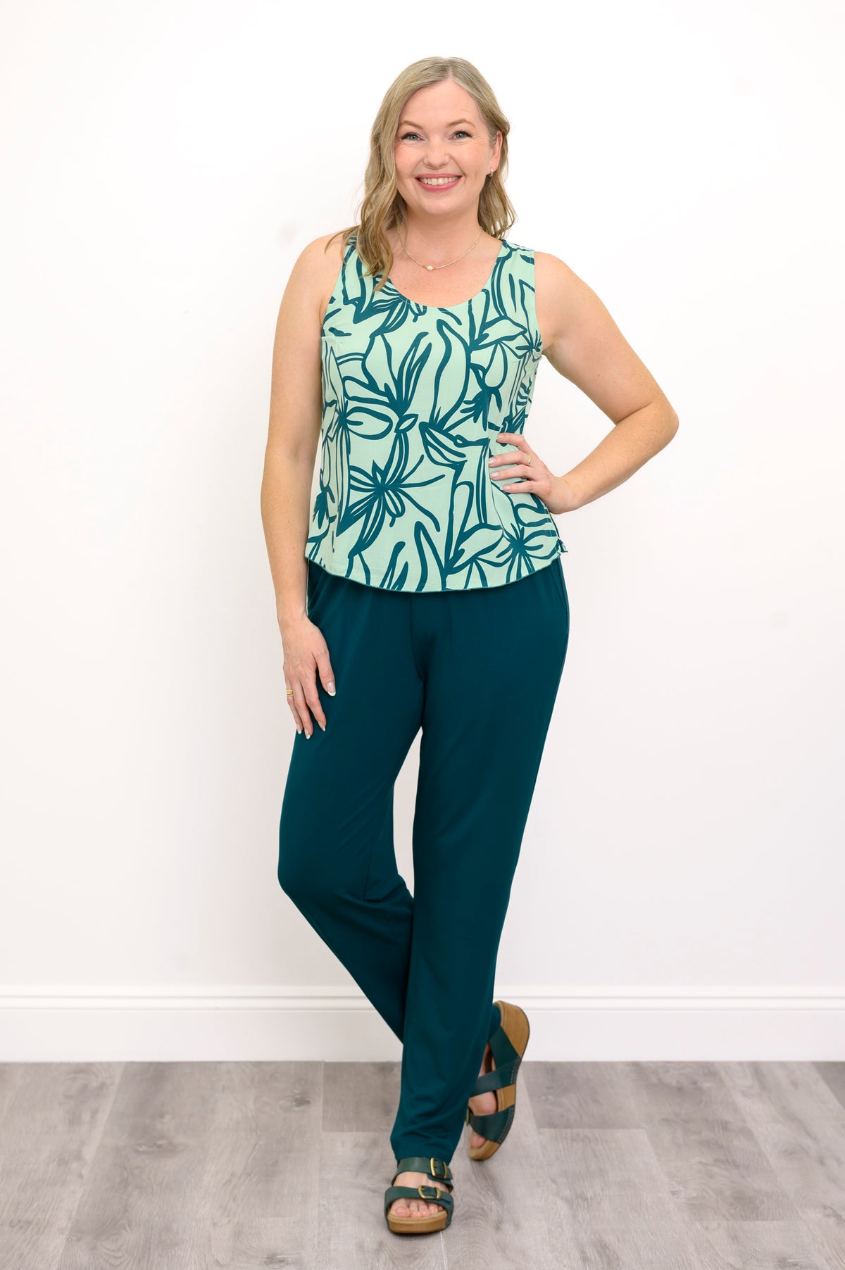 Front view of Woman wearing a green floral patterned sleeveless top and green pants against a white background