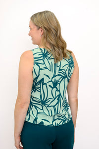 Back view of Woman wearing a green floral patterned sleeveless top and green pants against a white background