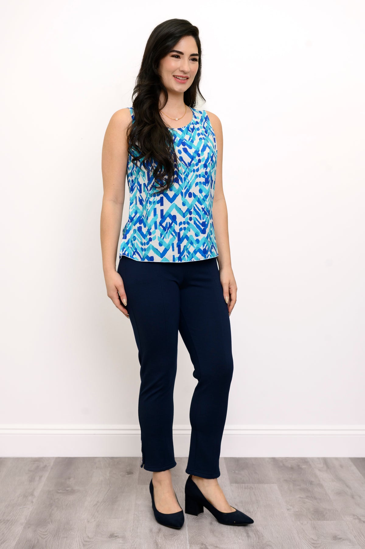 Front view of woman wearing a blue patterned sleeveless top and navy pants against a white background