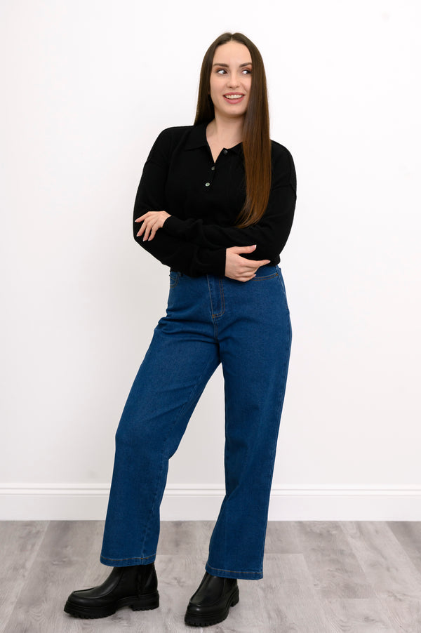 Woman standing in a black cashmere sweater, straight-leg jeans, and black boots