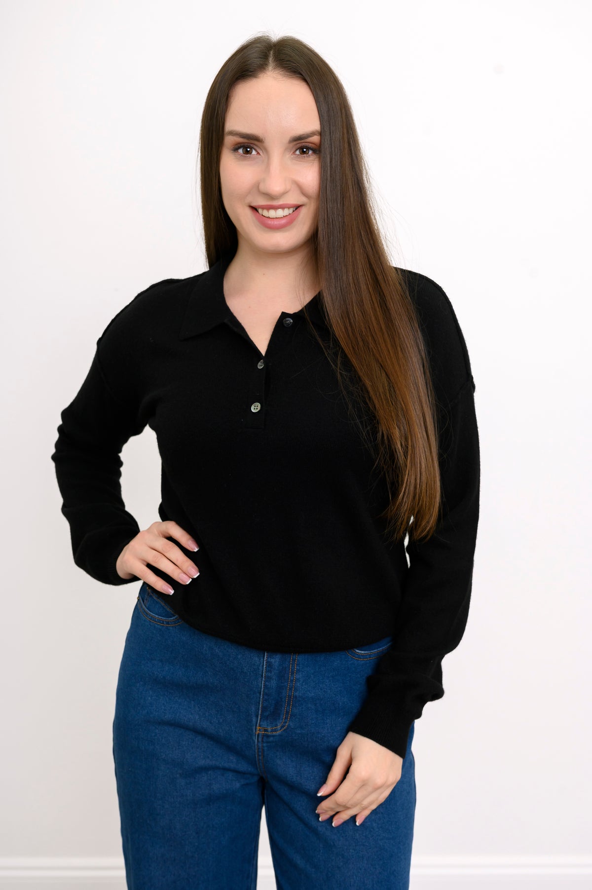 Woman wearing a black collared knit sweater and denim pants on a white background, front view