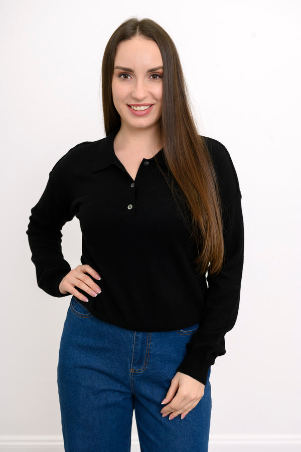 Woman wearing a black collared knit sweater and denim pants on a white background, front view