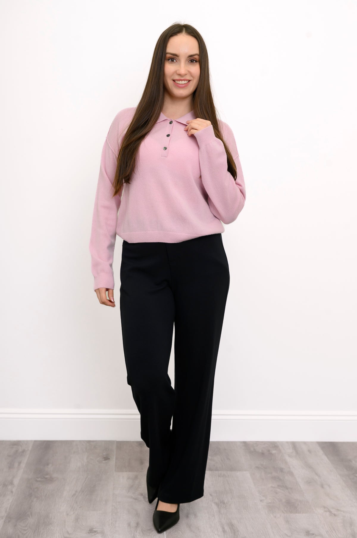 Woman posing with her hand on the collar of her button up blush pink cashmere sweater