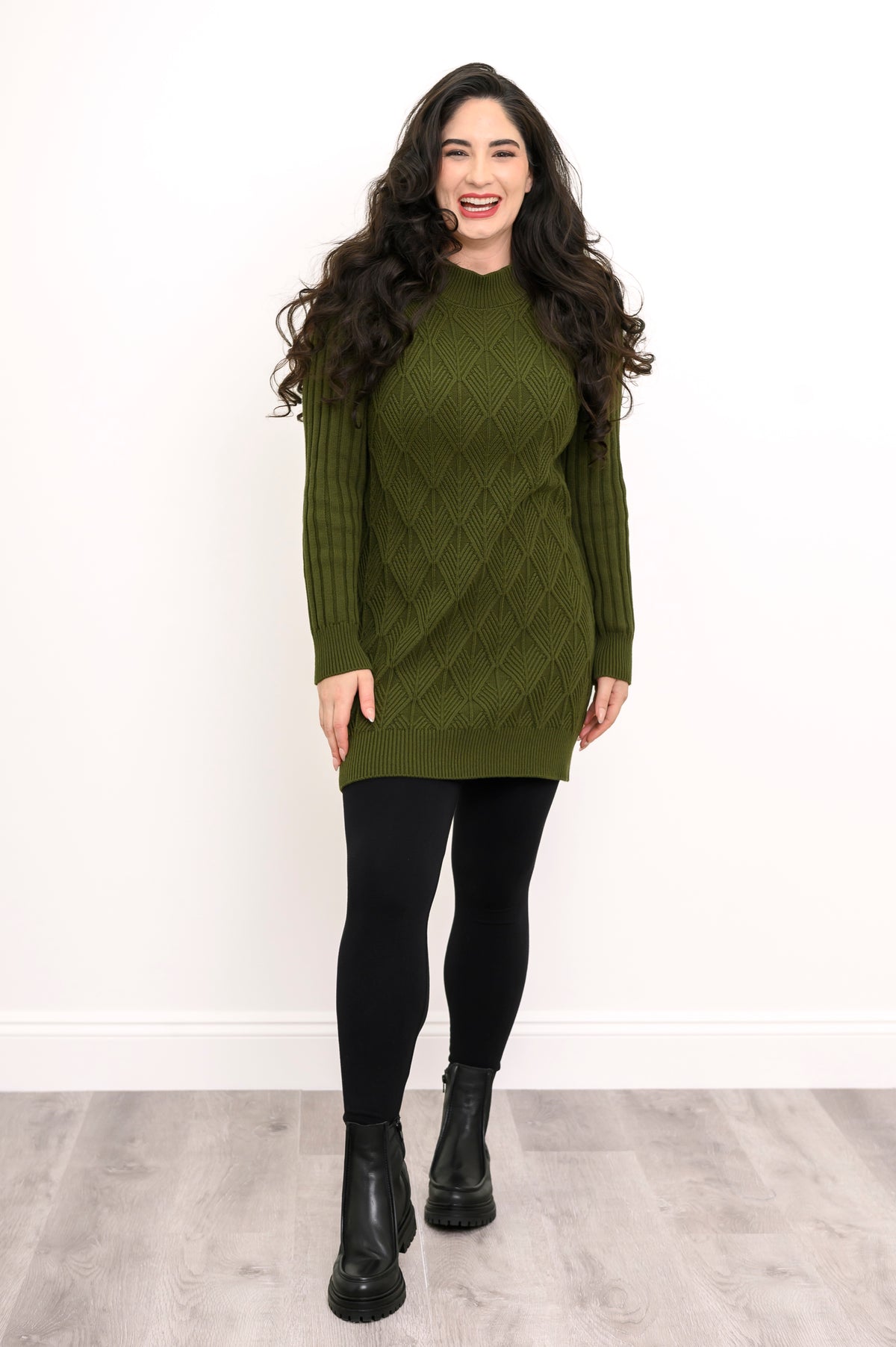 Full length shot of a woman wearing a vintage green cable knit tunic sweater styled with black boots.