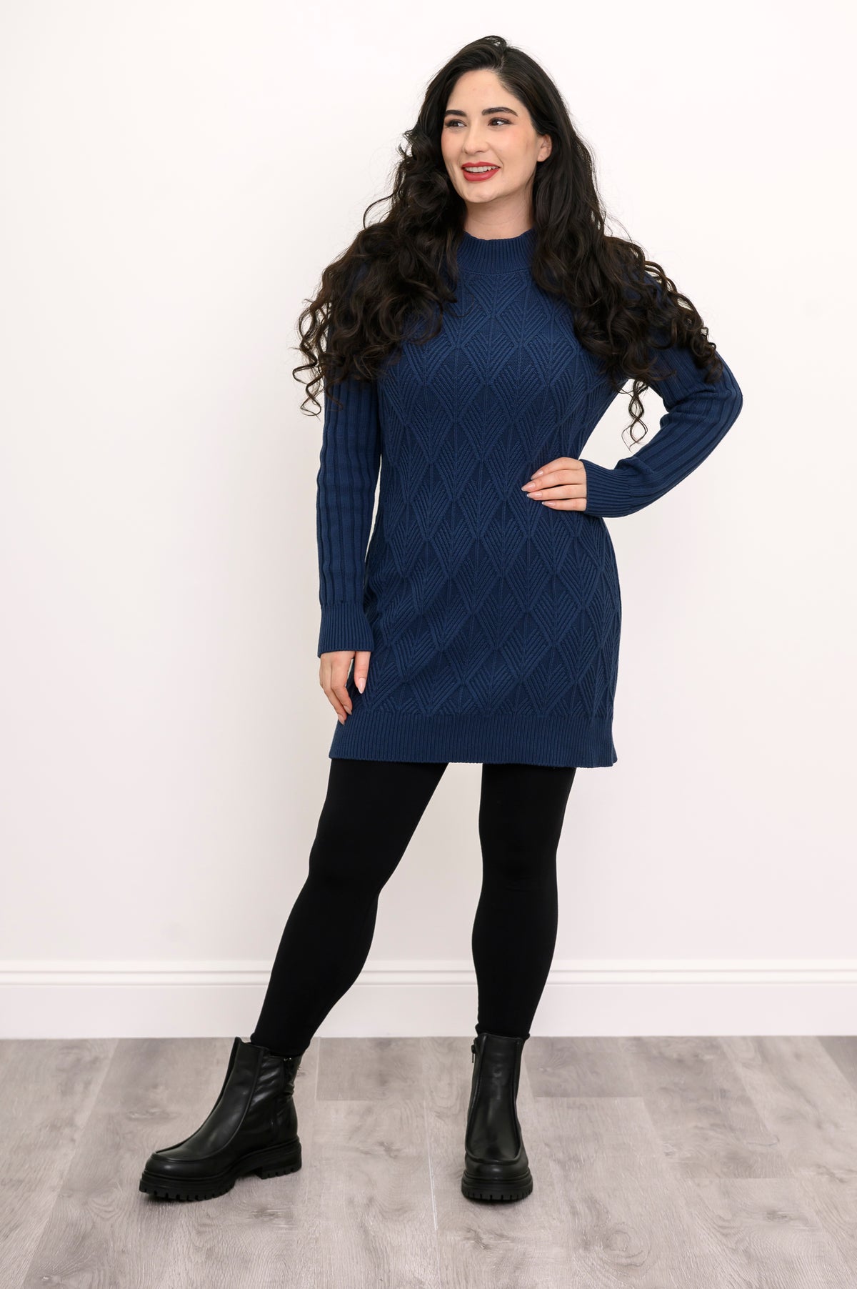 Woman in a longline dark blue cotton knit sweater featuring a wide banded hemline and dark leggings.