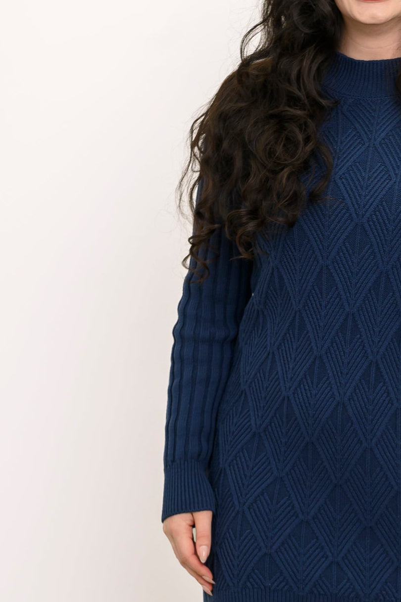 Side profile shot of a woman wearing a dark indigo long sleeve cable knit sweater tunic with boots.