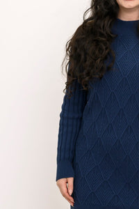Side profile shot of a woman wearing a dark indigo long sleeve cable knit sweater tunic with boots.