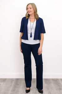 Front view, woman wearing navy blue jacket, white top, blue necklace, and blue pants against a white background