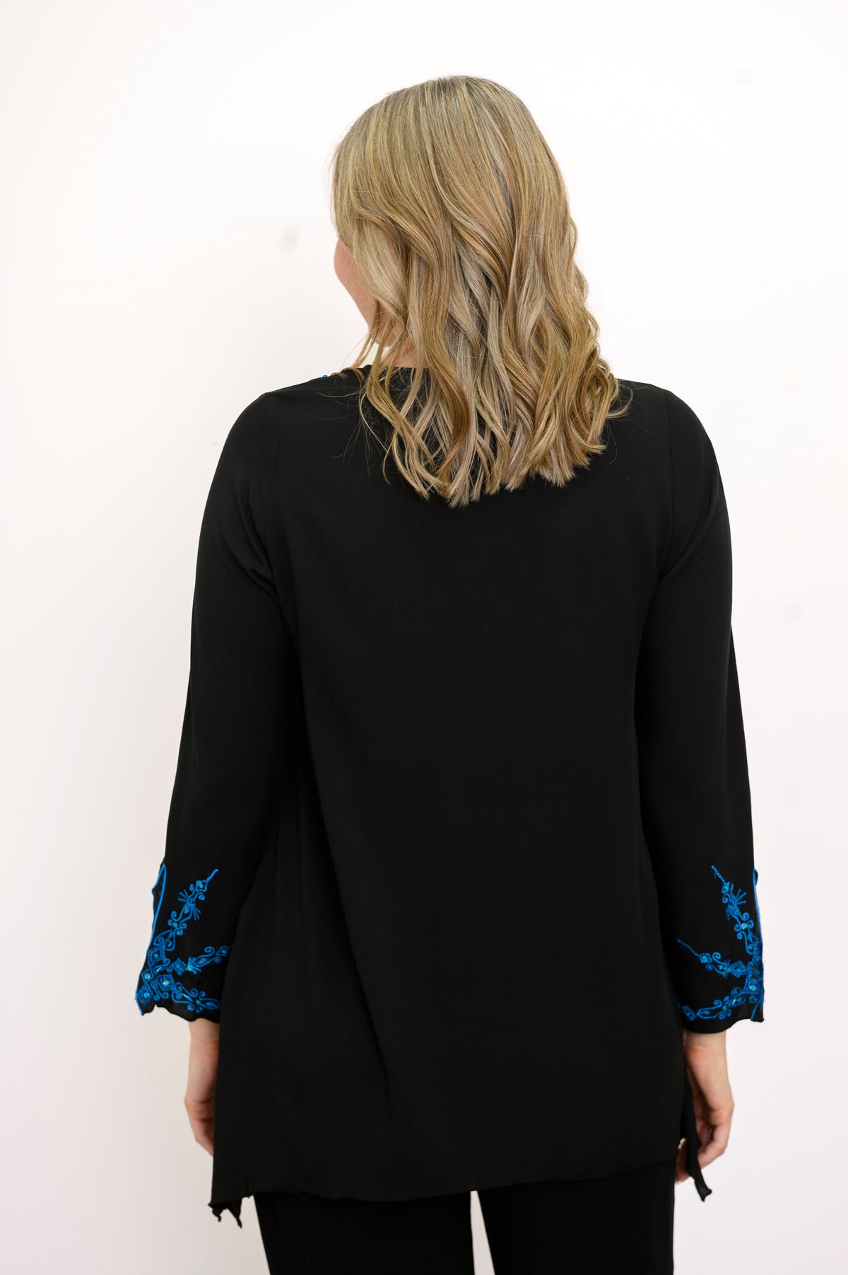 Back view of woman wearing a black top with blue embellishments and black pants against a white background