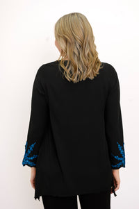 Back view of woman wearing a black top with blue embellishments and black pants against a white background