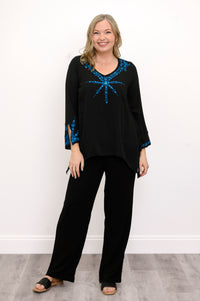Front view of woman wearing a black top with blue embellishments and black pants against a white background