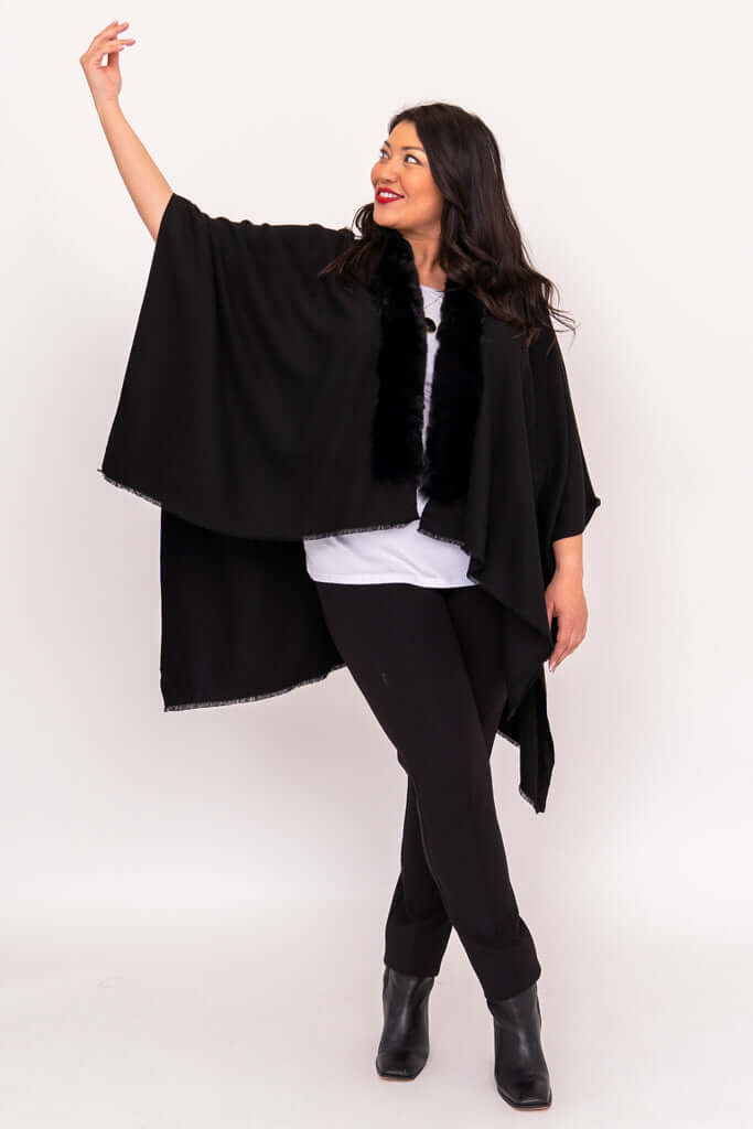 Woman posing in flowing black wrap with outstretched arm and faux fur collar