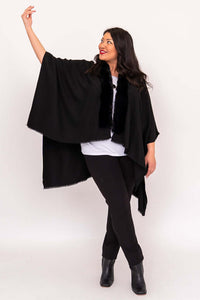 Woman posing in flowing black wrap with outstretched arm and faux fur collar