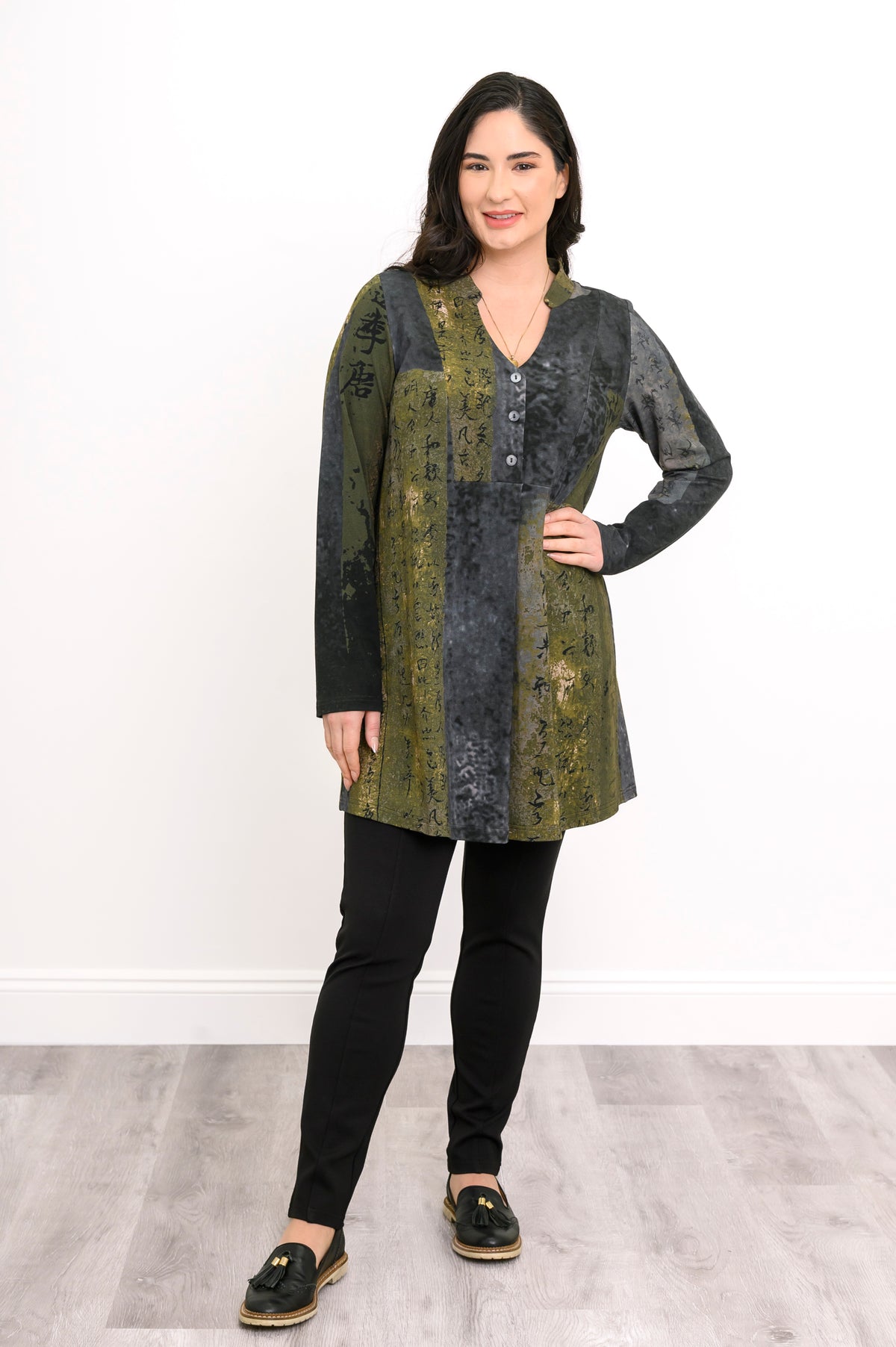 Model posing in a patterned olive-grey longline shirt with a buttoned collar and relaxed-fit long sleeves.