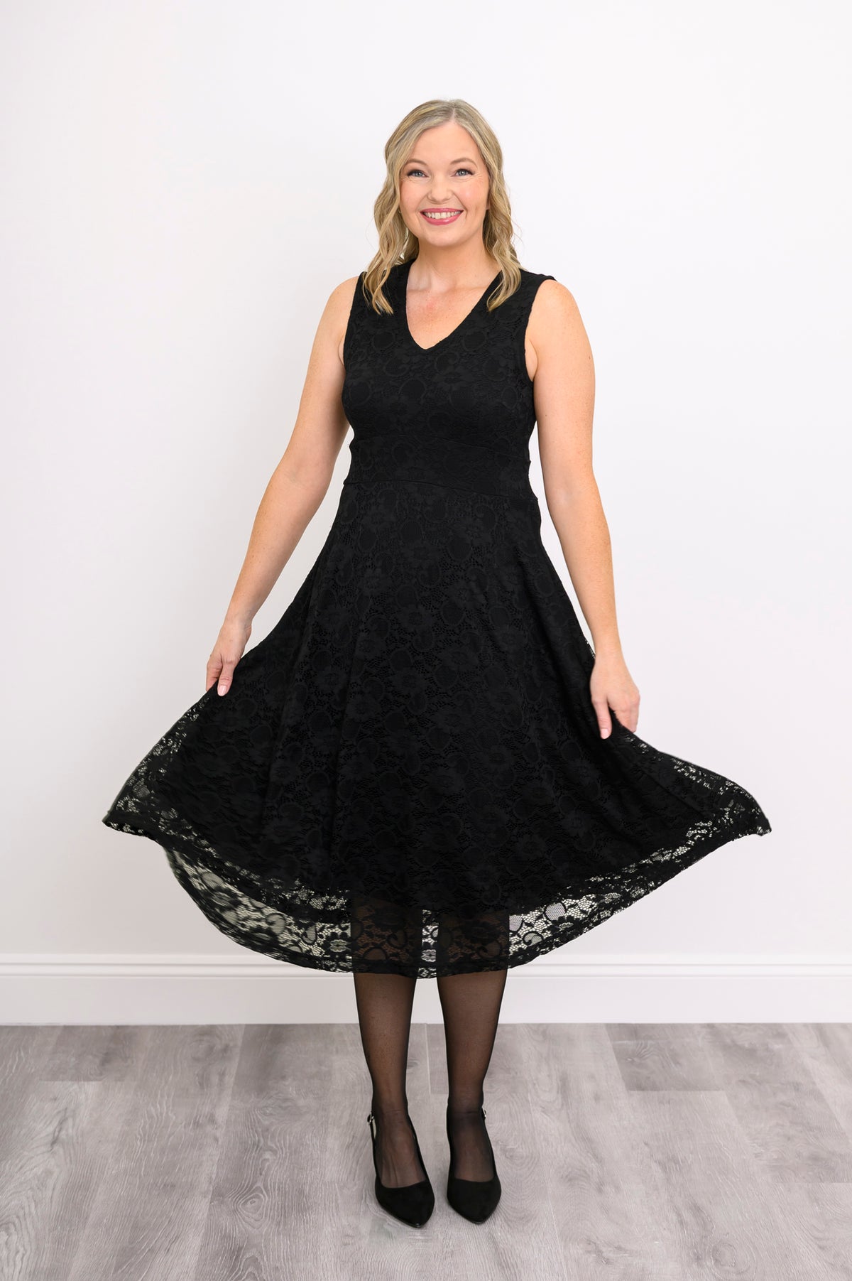 Woman playfully swaying her sleeveless black lace dress and smiling