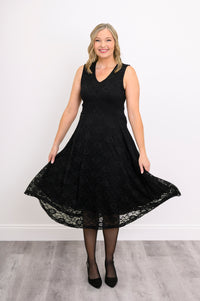Woman playfully swaying her sleeveless black lace dress and smiling