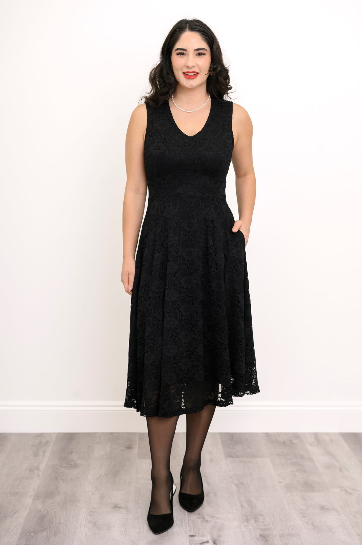 Full body front view of woman wearing black lace dress and posing with her hand in her pocket