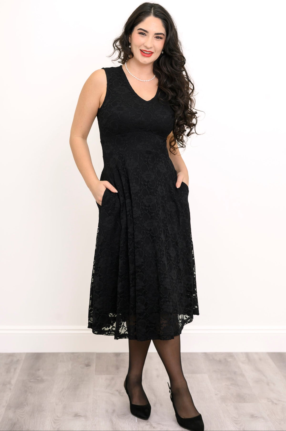 Woman wearing a black lace midi dress and black shoes against a white background, front view