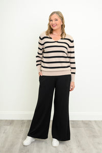 Smiling model posing in a classic black-striped cream sweater with long sleeves, standing in a front pose.